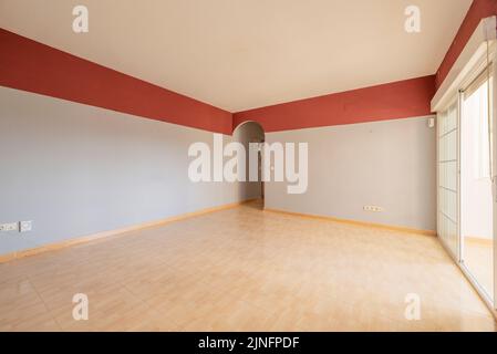 Empty room with gray walls and red band, painted cast-iron radiator and imitation wood stoneware floors, exit to a terrace and exit without a door wit Stock Photo