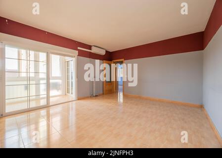 Empty room with gray walls and red band, painted cast iron radiator and imitation wood stoneware floors, exit to a glazed terrace and pine carpentry Stock Photo
