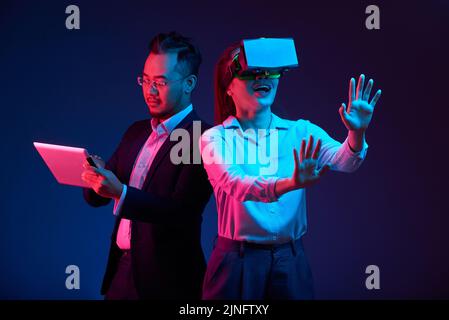 Businessman using app on tablet computer that controls VR headset on young woman Stock Photo