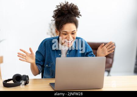 excited young African American woman celebrating success sitting with laptop at home or office Stock Photo