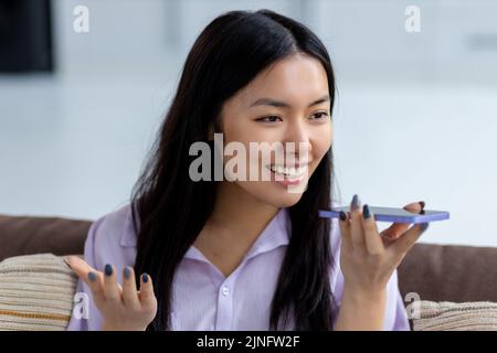 Young Asian woman sending voice message through using mobile phone smiling friendly Stock Photo