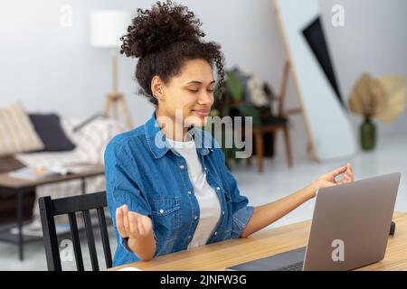 Calm African American young woman sitting workplace in the office and meditating taking break avoiding stressful job Stock Photo