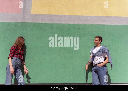 Beautiful couple hanging out and talking while leaning on the green wall Stock Photo