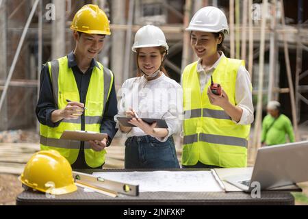 architector and engineers with draft plan of building and tablet computer talking on constructing site. Stock Photo