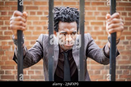 Behind Bars. A frustrated young business professional trapped behind iron bars. From a series of related images with the same model. Stock Photo