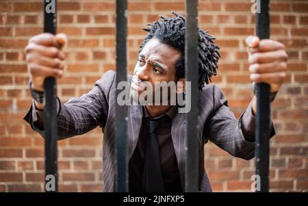 Behind Bars. A frustrated young business professional trapped behind iron bars. From a series of related images with the same model. Stock Photo