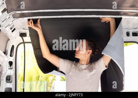 Young man working placing and sticking the rubber isolation in the camper van convertion. As a profession service Stock Photo