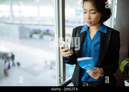 Young Vietnamese business lady with plane ticket reading message on her smartphone Stock Photo