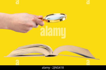 Hand holding magnifying glass over open book on yellow background. Conducting research, information analysis, data search concept. High quality photo Stock Photo