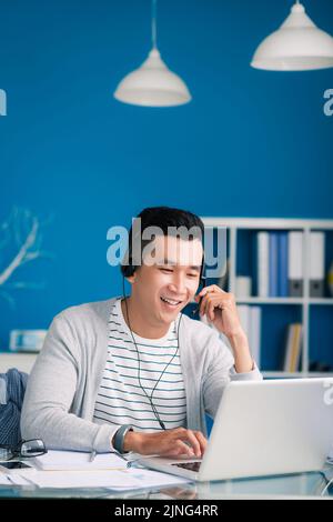 Happy Asian businessman in headset talking to client Stock Photo