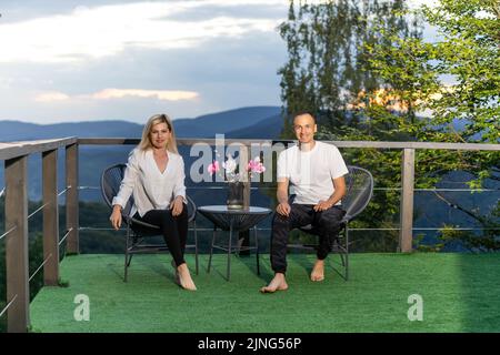 Horizontal sideview shot of a young couple in summer outfit enjoying the mountain view from terrace. Copy space. Stock Photo