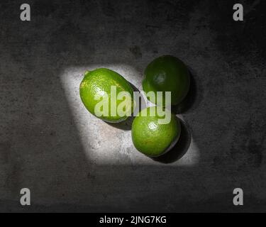 Close up of three bright green limes against a concrete background. Stock Photo