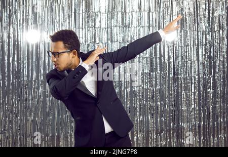 Happy confident black man in a tuxedo suit and glasses dancing and having fun at a party Stock Photo