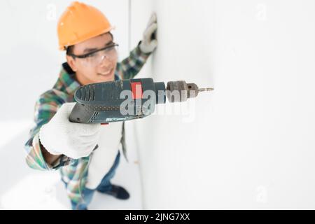 Cheerful young Vietnamese man drilling hole in a wall Stock Photo