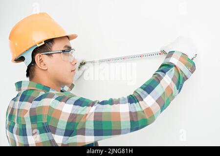 Young Asian man in helmet measuring wall Stock Photo