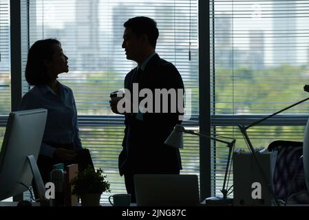 Cheerful colleagues talking during break in dark office Stock Photo