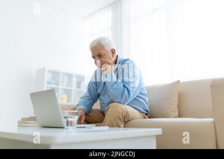 Sad pensive senior man reading e-mails on his laptop Stock Photo