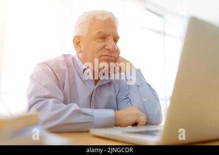 Sad aged man reading e-mails on laptop Stock Photo