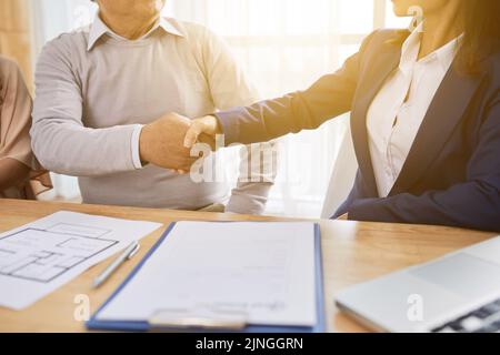 Close-up shot of unrecognizable senior man and estate agent shaking hands after successful completion of meeting, purchase agreement lying on table Stock Photo