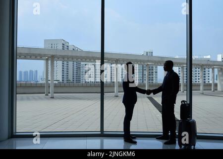 Business people standing against big airport window and shaking hands Stock Photo