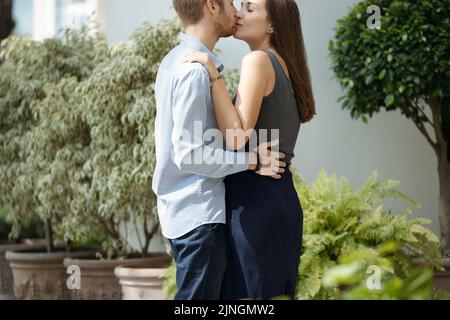Beautiful young couple kissing near decorative potted plants Stock Photo