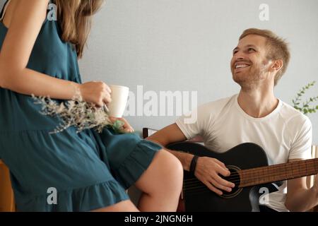 Charismatic young man playing guitar for his girlfriend at home Stock Photo
