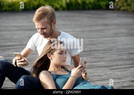Young couple using their smartphones while spending time together outdoors Stock Photo