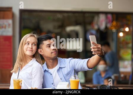 Young mixed couple taking selfie with smartphone at outdoor cafe Stock Photo