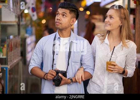 Young mixed couple of tourists walking down street and looking around Stock Photo