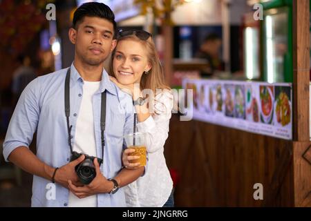 Young mixed couple of tourists looking at camera, man carrying camera Stock Photo