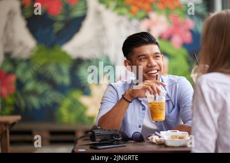 Cheerful Asian man chatting with his Caucasian girlfriend at cafe Stock Photo