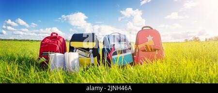 Children's schoolbags of different colours standing on the green field Stock Photo
