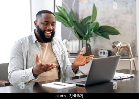 Online video conference, briefing. Positive friendly confident african american man, owner company, sales manager, sits on office, has business conversation with colleagues by video call using laptop Stock Photo