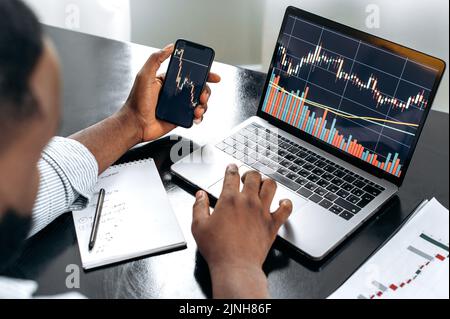 Crypto trader investor broker using cellphone and laptop for cryptocurrency financial market analysis, buying or selling cryptocurrency. Close-up of a laptop and cellphone screen with stock diagrams Stock Photo