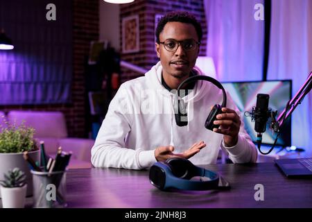 POV of male blogger recommending modern headphones, doing product review in recording studio. Lifestyle influencer filming with headset using podcast and live broadcast equipment. Stock Photo