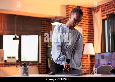 Young smiling african american businesswoman closing laptop at modern home office workplace. Female professional freelancer taking rest break at work in contemporary coworking room Stock Photo