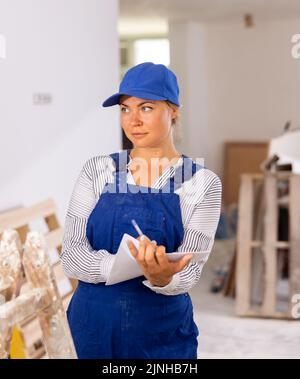 Female foreman in blue workwear making task list in building under construction Stock Photo