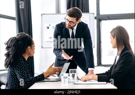 Elegant Caucasian intelligent male boss, holding group brainstorm with female colleagues, discussing ideas for a new business project, analyzes report and profit, explain info Stock Photo