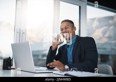 You can trust him to keep your business in safe hands. a handsome young businessman talking on a cellphone while working in an office. Stock Photo
