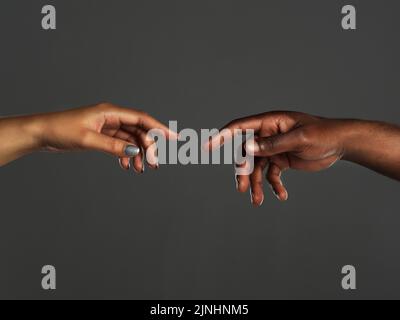 In touching distance. Studio shot of two unrecognizable people reaching out their hands towards each other against a grey background. Stock Photo