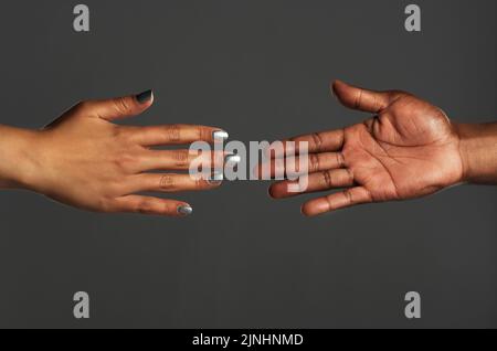 Reaching out for help is an act of strength. Studio shot of two unrecognizable people reaching out their hands towards each other against a grey Stock Photo