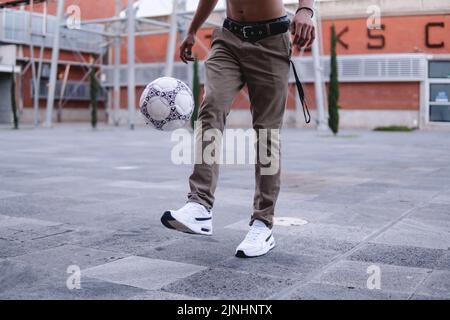 Unrecognizable man dominating his soccer ball in a city square and with buildings in the background. Legs of an athlete playing with the ball. Hispanic boy with ball in the air. High quality photo Stock Photo