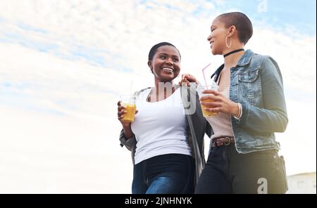 Making our way down town. Low angle shot of two young women walking in the city laughing while holding their cool drinks. Stock Photo