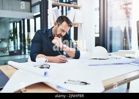Working hard to meet his clients needs. a mature male architect working on a design in his office. Stock Photo
