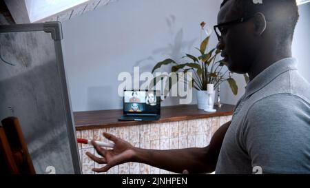 An online lesson - an african-american man teacher standing by the board and explains the material for his students on the screen Stock Photo