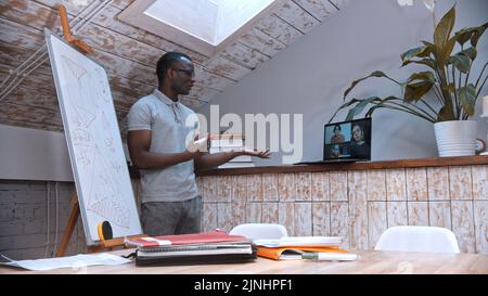 An online lesson - an african-american man teacher in glasses standing by the board and explains the material for his students on the screen Stock Photo