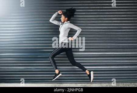 Find your fire and then run with it. a sporty young woman running against a grey background. Stock Photo