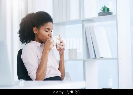 My systems just needs a few sips. a young businesswoman drinking a cup of coffee in an office. Stock Photo