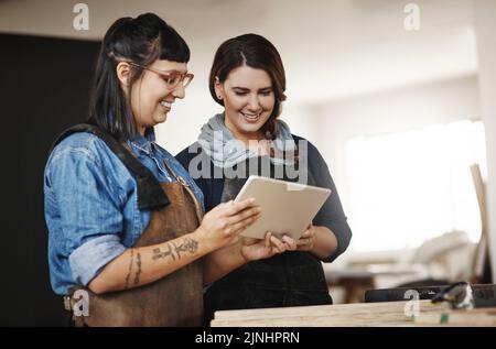These are the designs Ive been working on. two attractive young creative female artisans working on a tablet in their workshop. Stock Photo