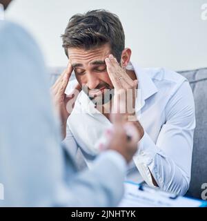 Its a lot to process right now. an stressed out young man having a discussion with his doctor while being seated on a sofa inside of a doctors office Stock Photo